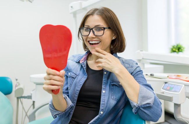 Young woman holding a mirror at home practicing Austin home dental care tips