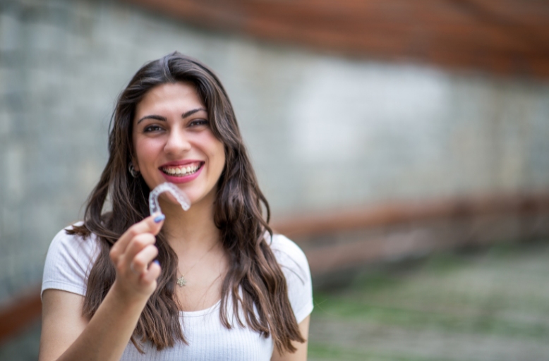 Smiling woman holding clear aligner tray demonstrating Invisalign treatment for teeth straightening and clear aligners in Austin TX